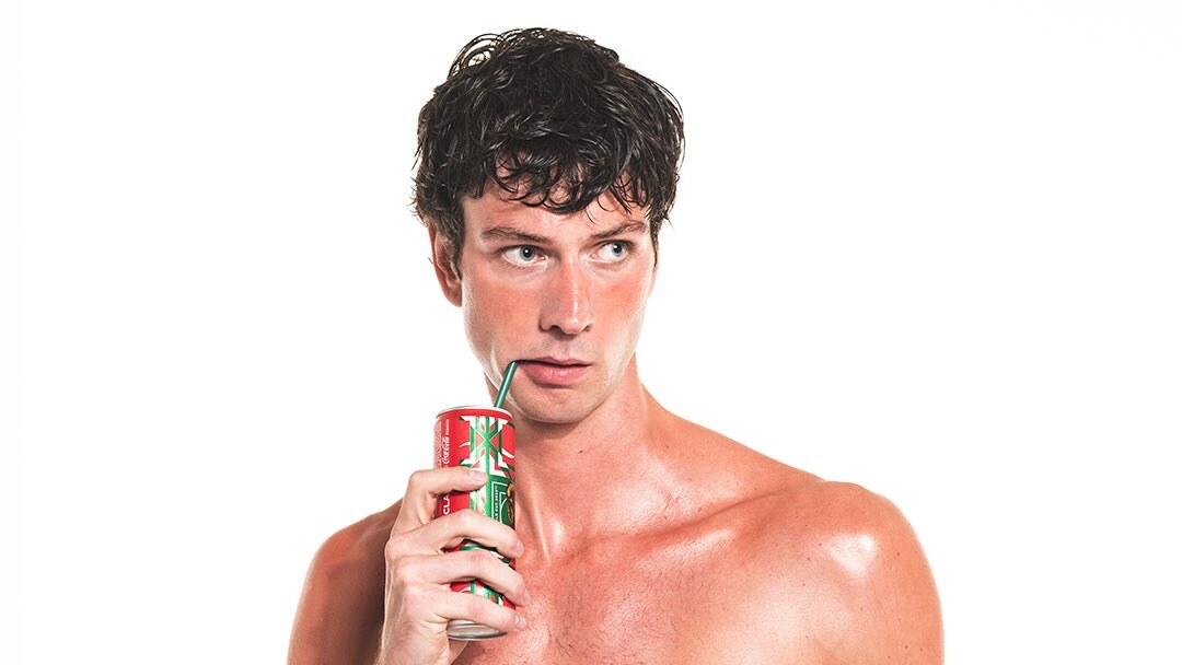 Eike Nink poses shirtless against a white background while drinking from a can through a straw.