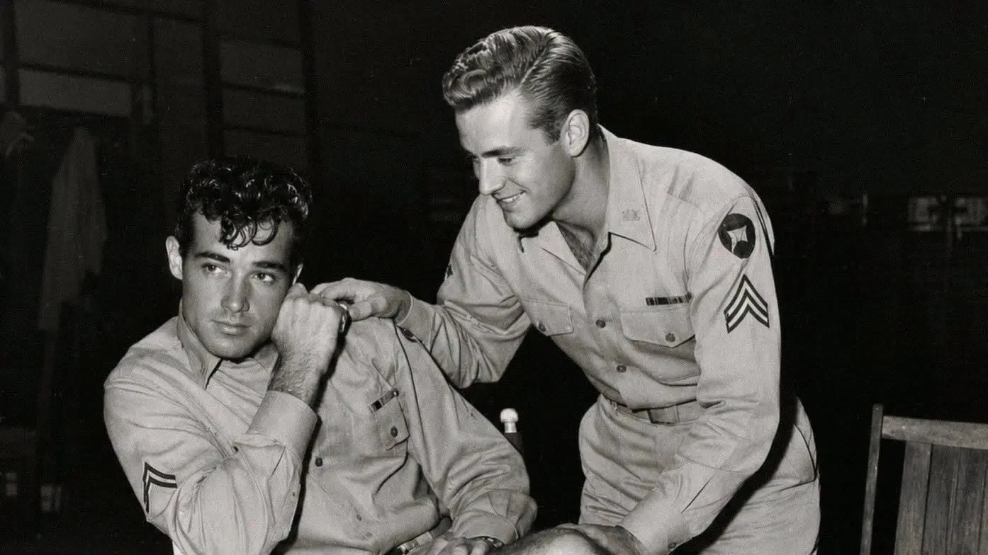 Guy Madison and Bill Williams pose in military uniforms, with Madison seated in a director's chair and Williams standing beside him.